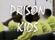 Young inmates in yellow prison uniforms sitting together.