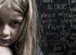A young girl with messy hair looks sad in front of a blackboard with emotional writing.