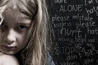 CHILD VIOLENCE1 A young girl with messy hair looks sad in front of a blackboard with emotional writing.