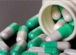 Green and white capsules spilling out of a white bottle.