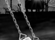 Empty swing hanging in a dark, moody playground at night.