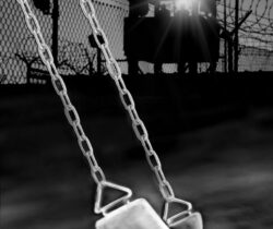 Empty swing hanging in a dark, moody playground at night.