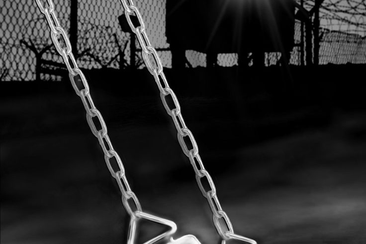 Empty swing hanging in a dark, moody playground at night.