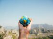 Hand holding a small globe with mountains in the background.