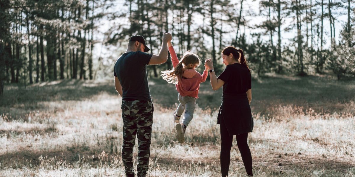 pexels-alexandr-podvalny-7911933 Parents lifting their child joyfully in a forest clearing.