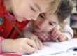 Two children focused on writing in a notebook together.