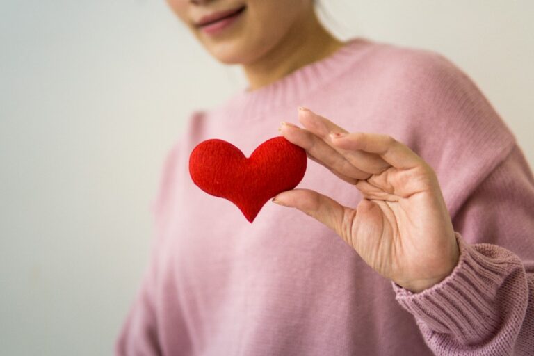 Person holding a small red heart in hand.