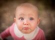 Close-up of a curious baby with big blue eyes and a pink outfit.