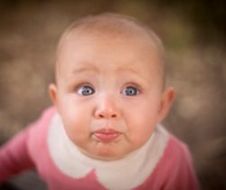 Close-up of a curious baby with big blue eyes and a pink outfit.