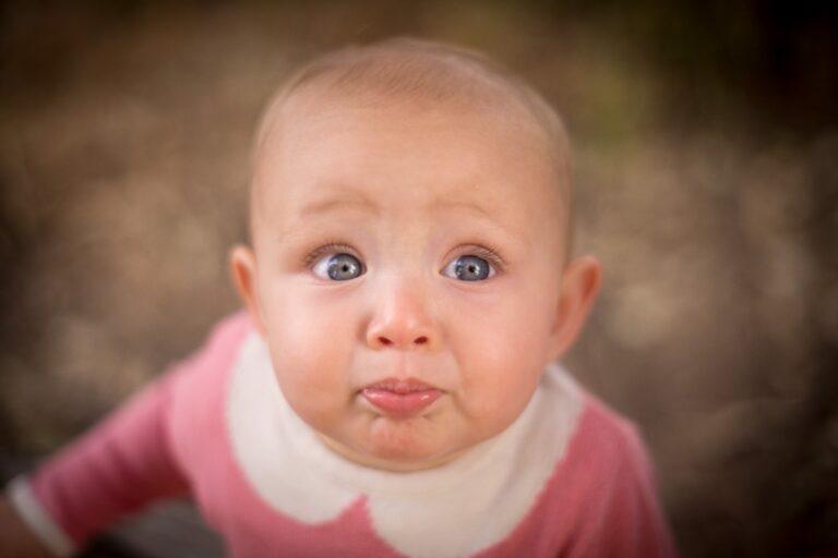 Close-up of a curious baby with big blue eyes and a pink outfit.