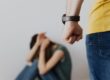 Man raising fist while woman cowers on floor, symbolizing domestic violence.