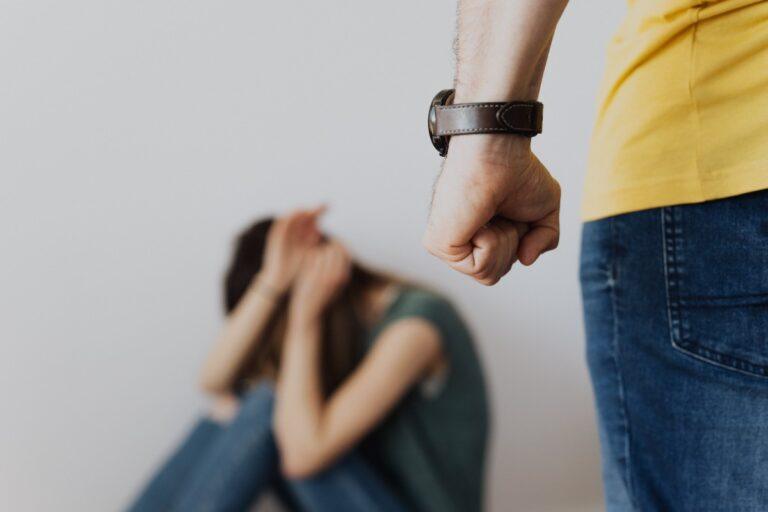 Man raising fist while woman cowers on floor, symbolizing domestic violence.