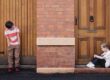 Two children playing outside near a brick building and wooden door.