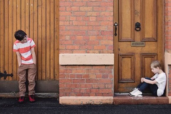 Two children playing outside near a brick building and wooden door.